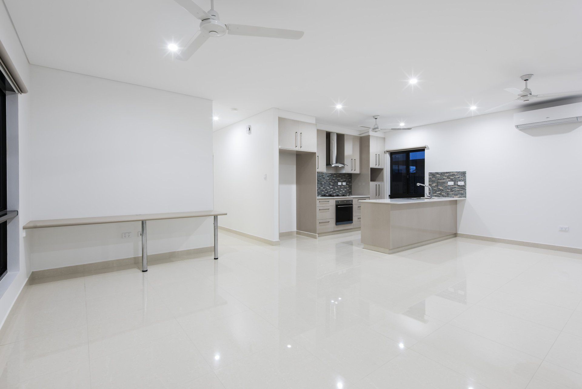 An empty living room with a ceiling fan and a kitchen.