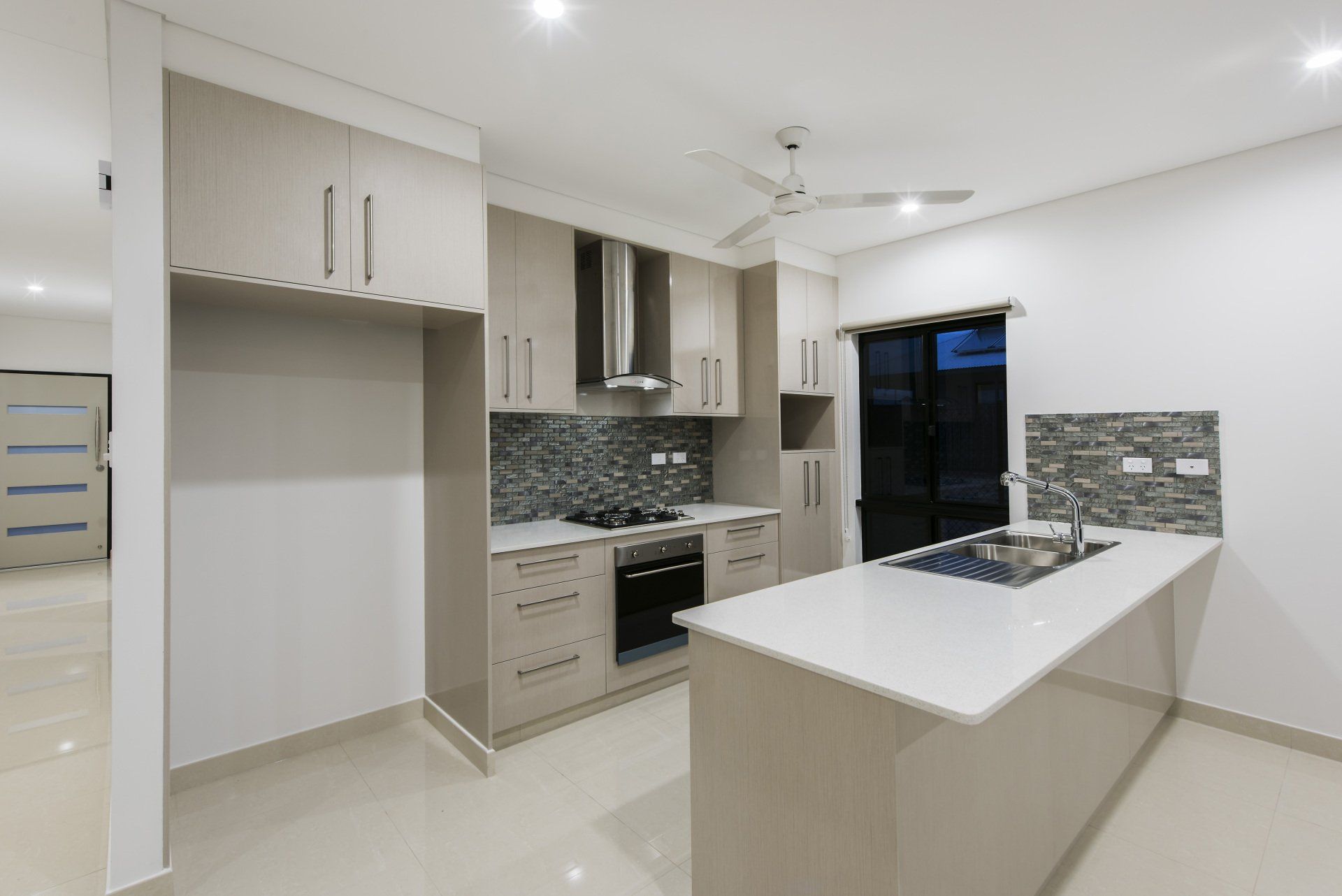A kitchen with a stove , sink , cabinets and a ceiling fan.