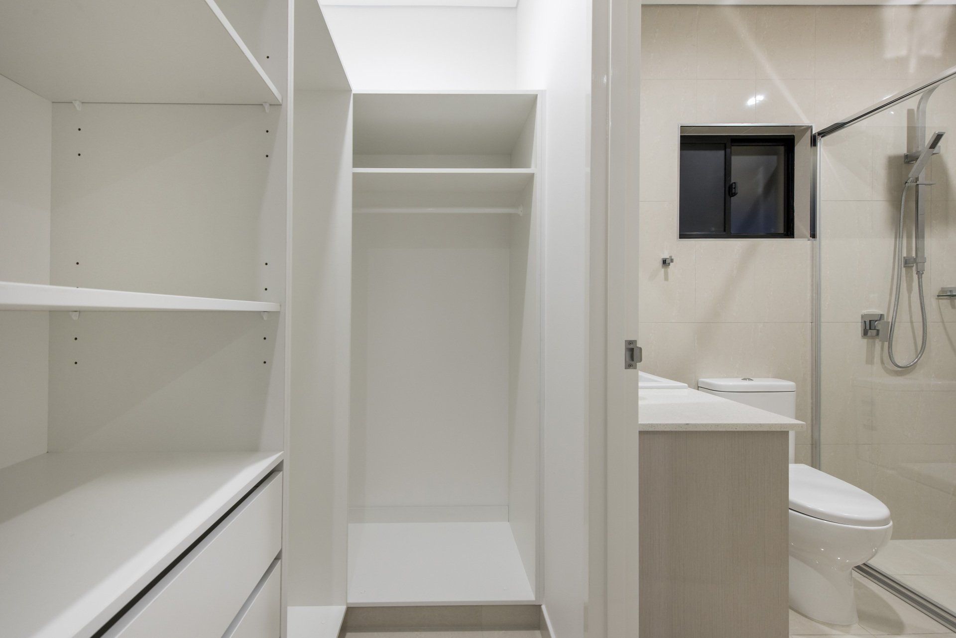A walk in closet next to a bathroom with a toilet and shower.