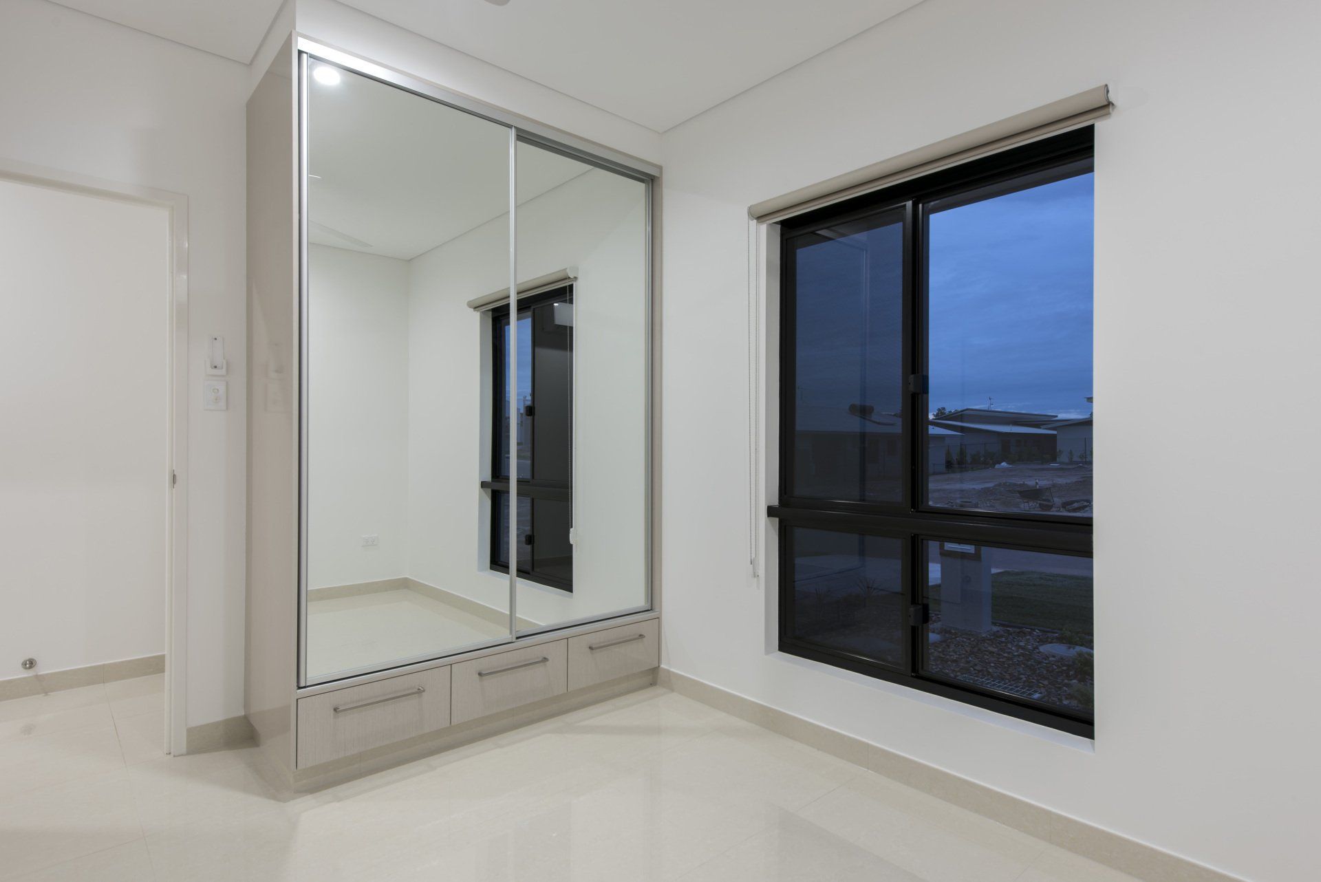 An empty bedroom with a large mirrored wardrobe and two windows.