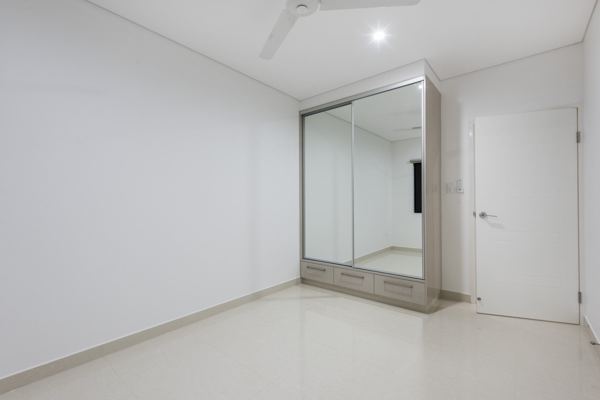 An empty bedroom with a large mirrored wardrobe and a ceiling fan.