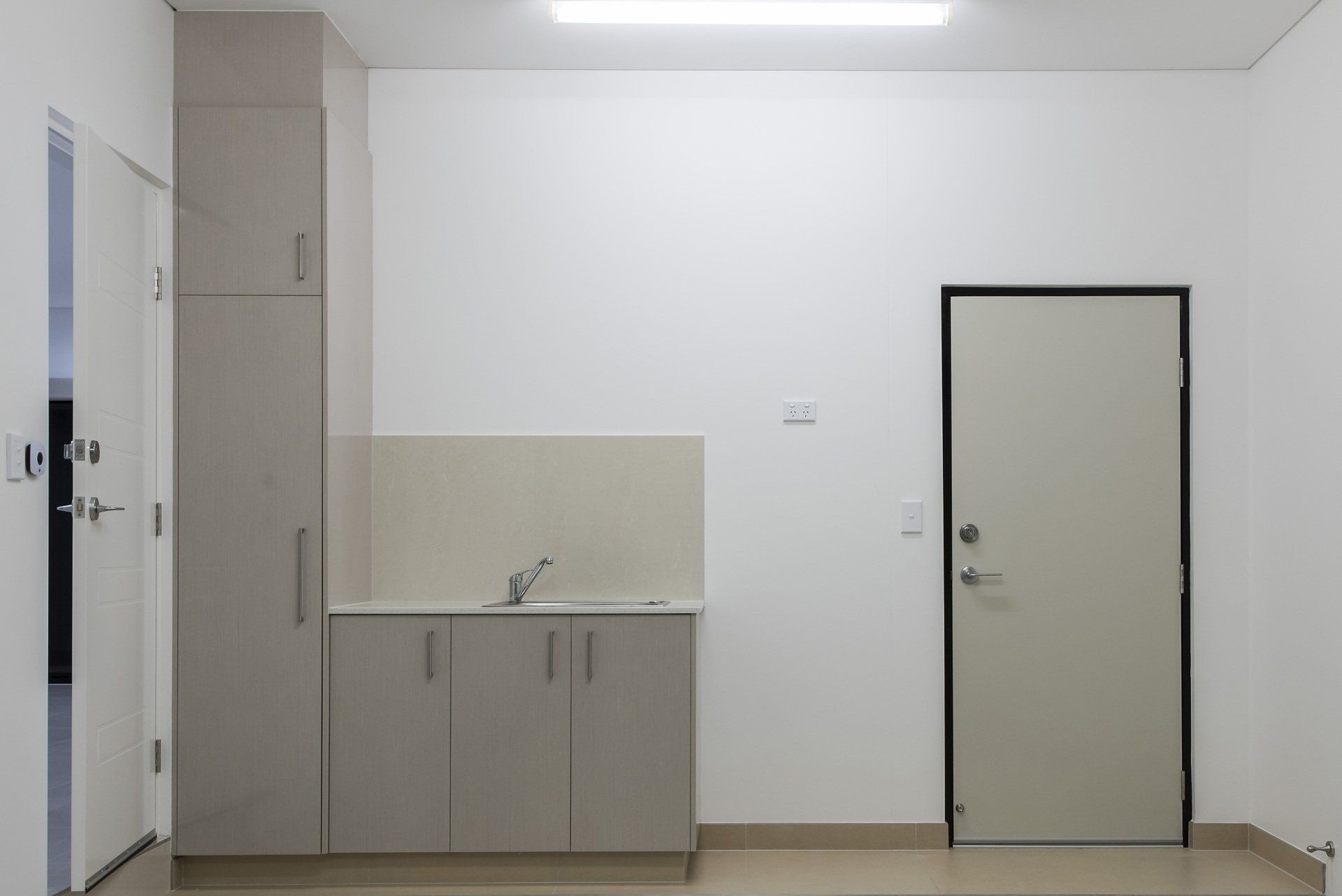 An empty room with a sink , cabinets , and a door.