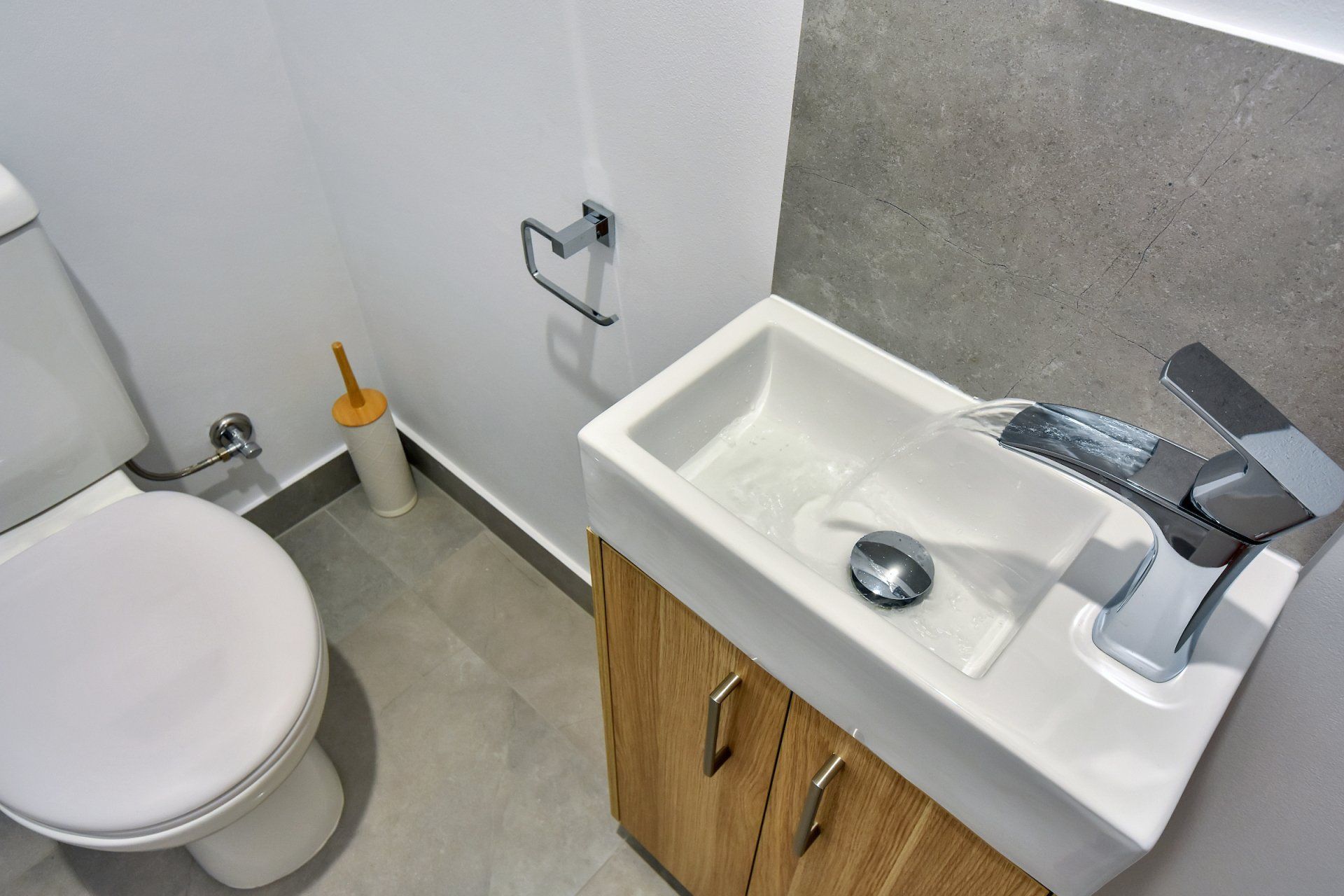 A toilet and sink in a bathroom with a wooden cabinet
