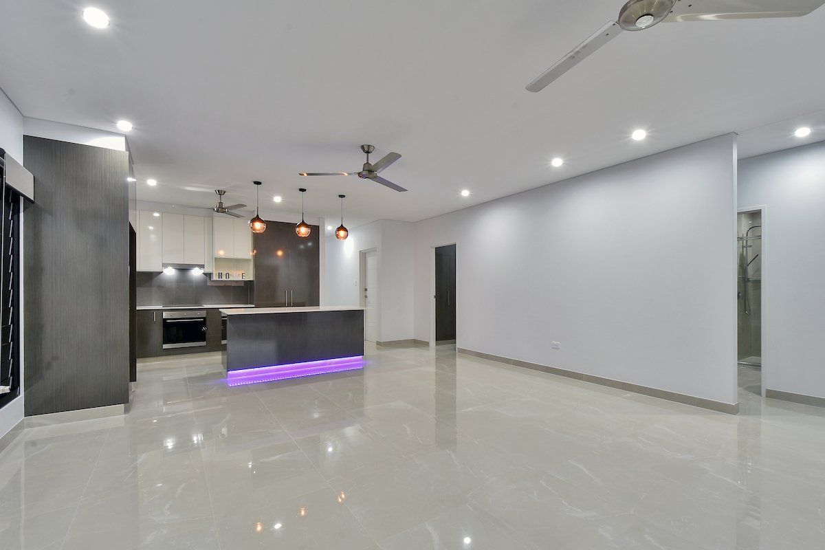 A large empty room with a kitchen and a ceiling fan.