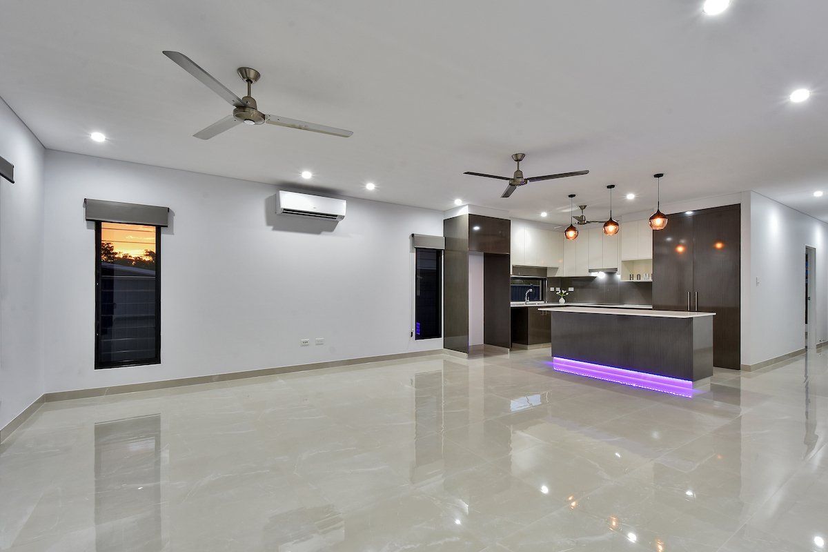 A large empty room with a ceiling fan and a kitchen