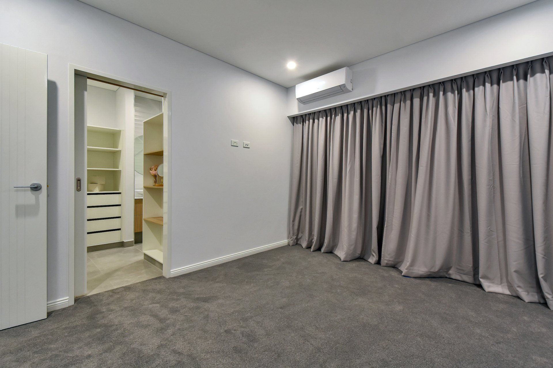 An empty bedroom with a walk in closet and curtains.