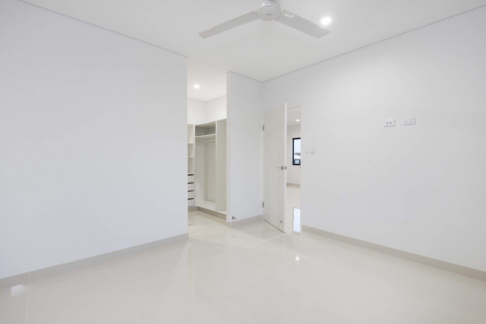 An empty room with white walls and a ceiling fan.
