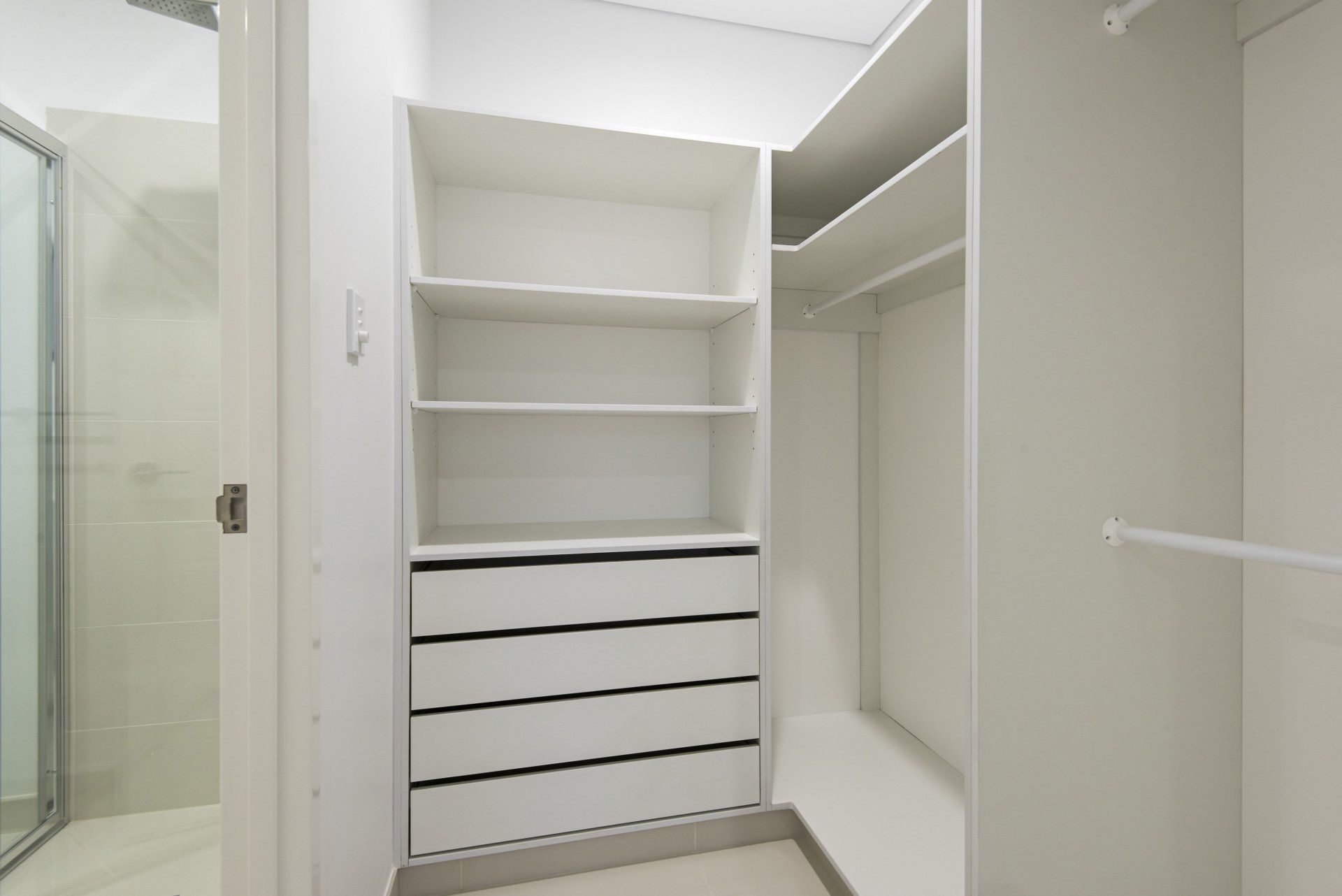 A walk in closet with lots of shelves and drawers next to a bathroom.