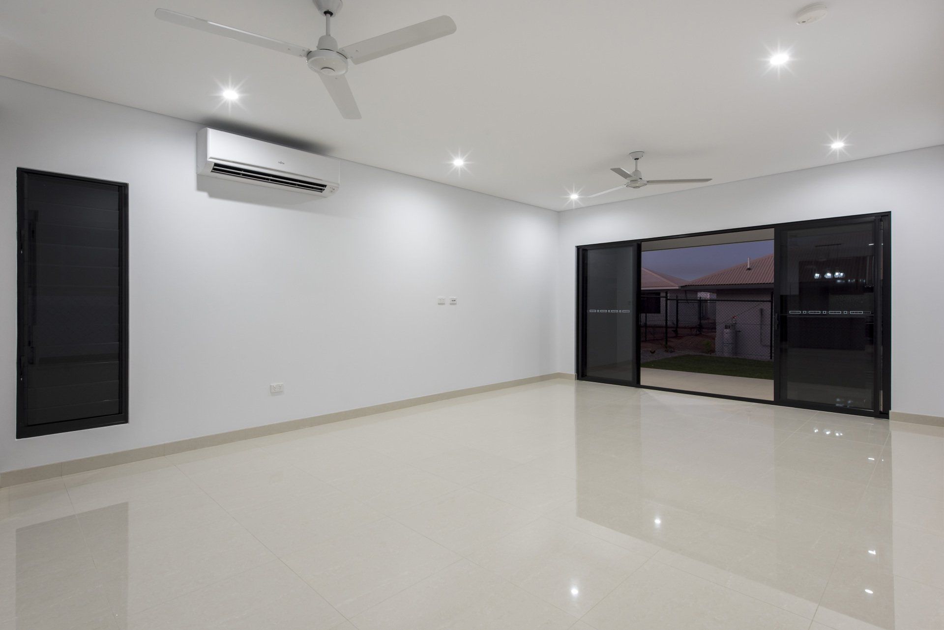 An empty living room with a ceiling fan and sliding glass doors.