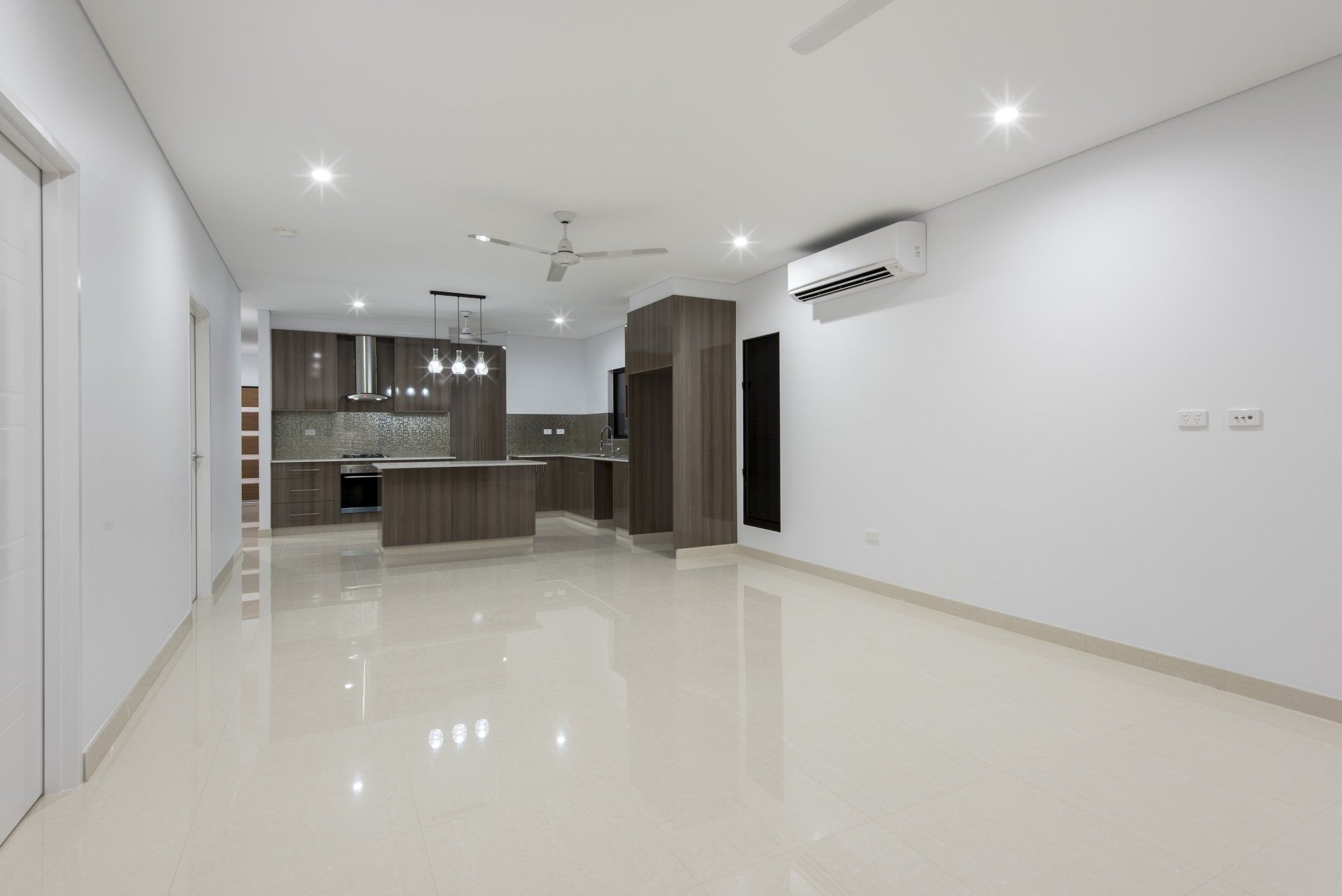 An empty living room with a kitchen in the background