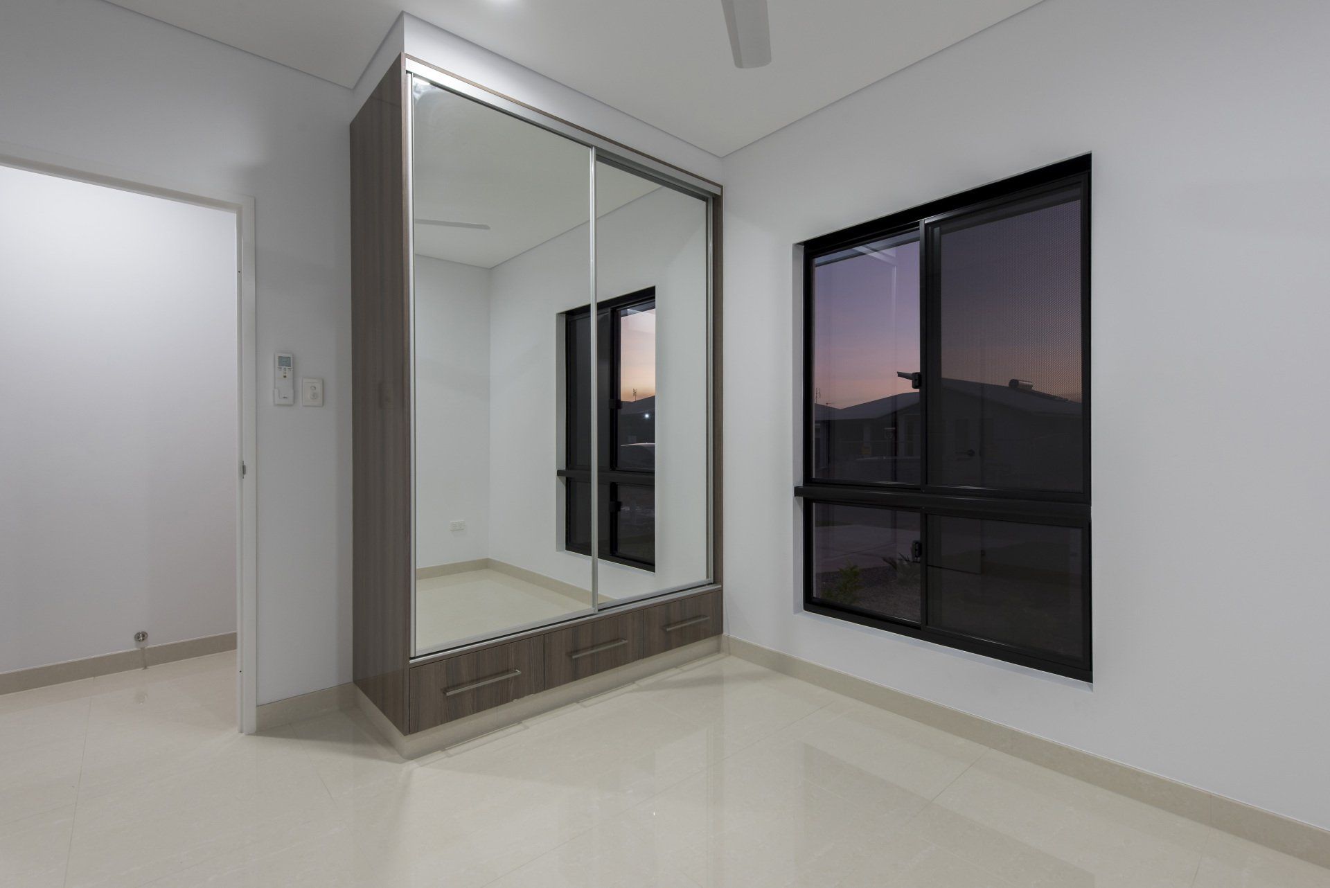An empty bedroom with a large wardrobe and two windows.
