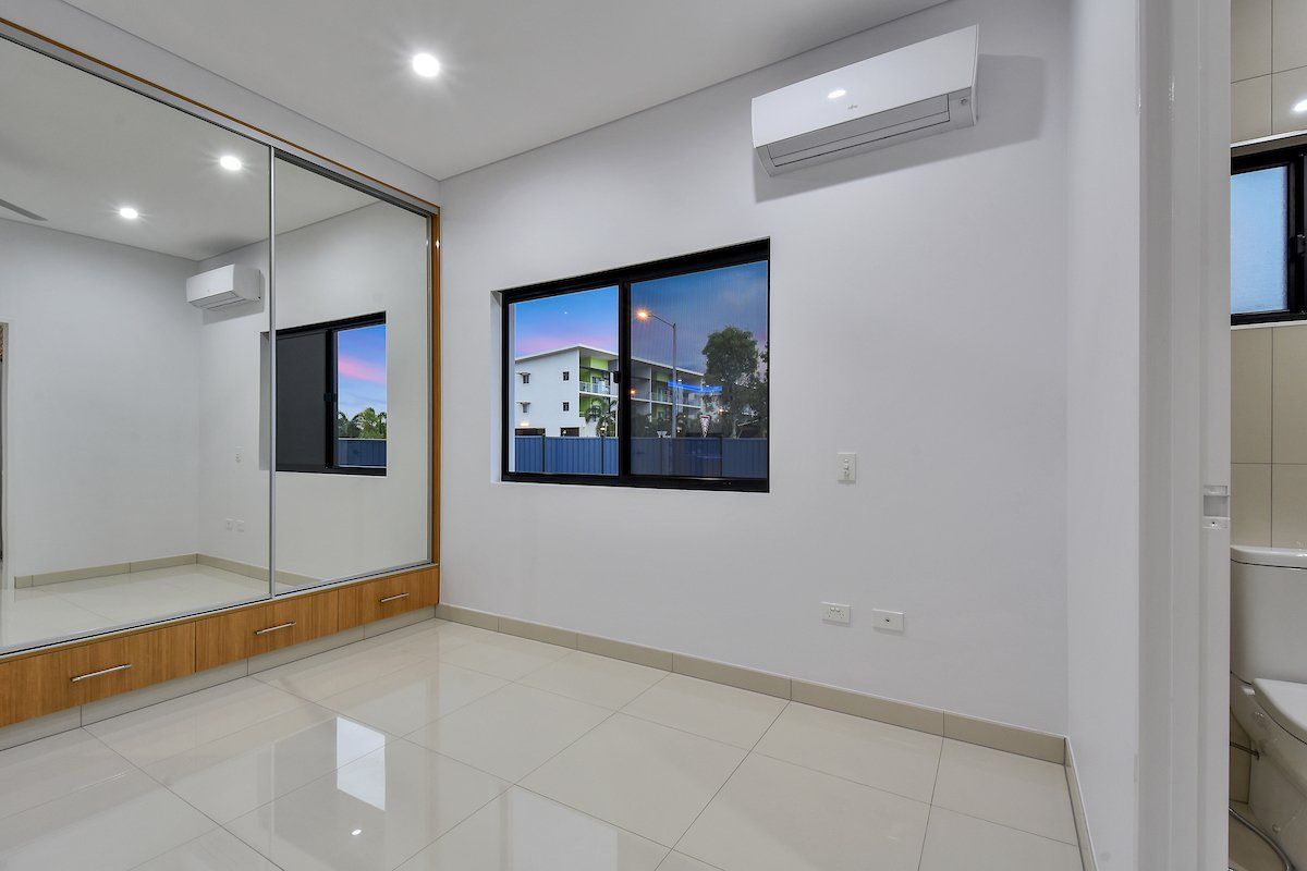 An empty bedroom with a large mirror on the wall and two windows.