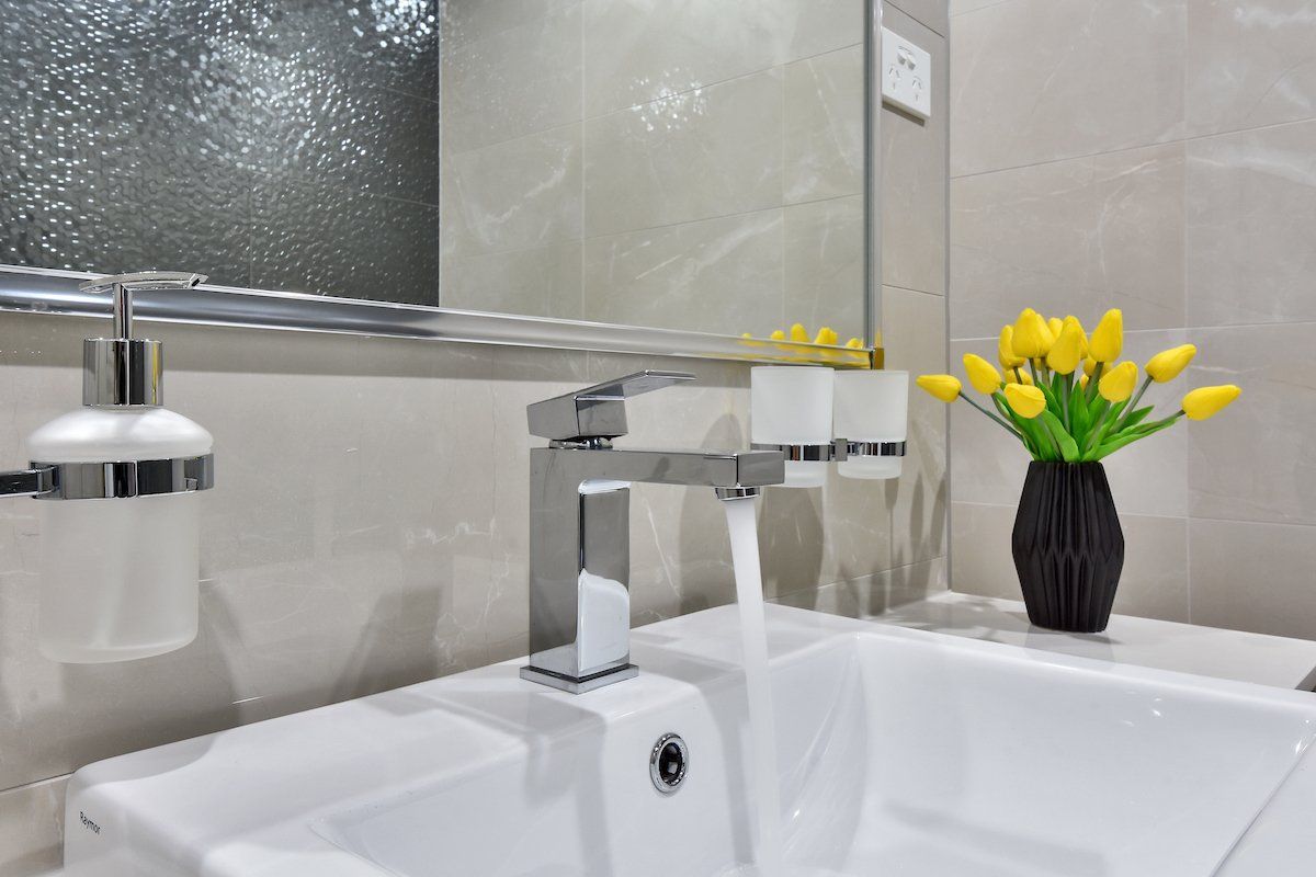 A bathroom sink with a vase of yellow flowers and a mirror.