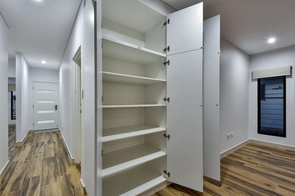 An empty closet in a hallway with wooden floors and a window.