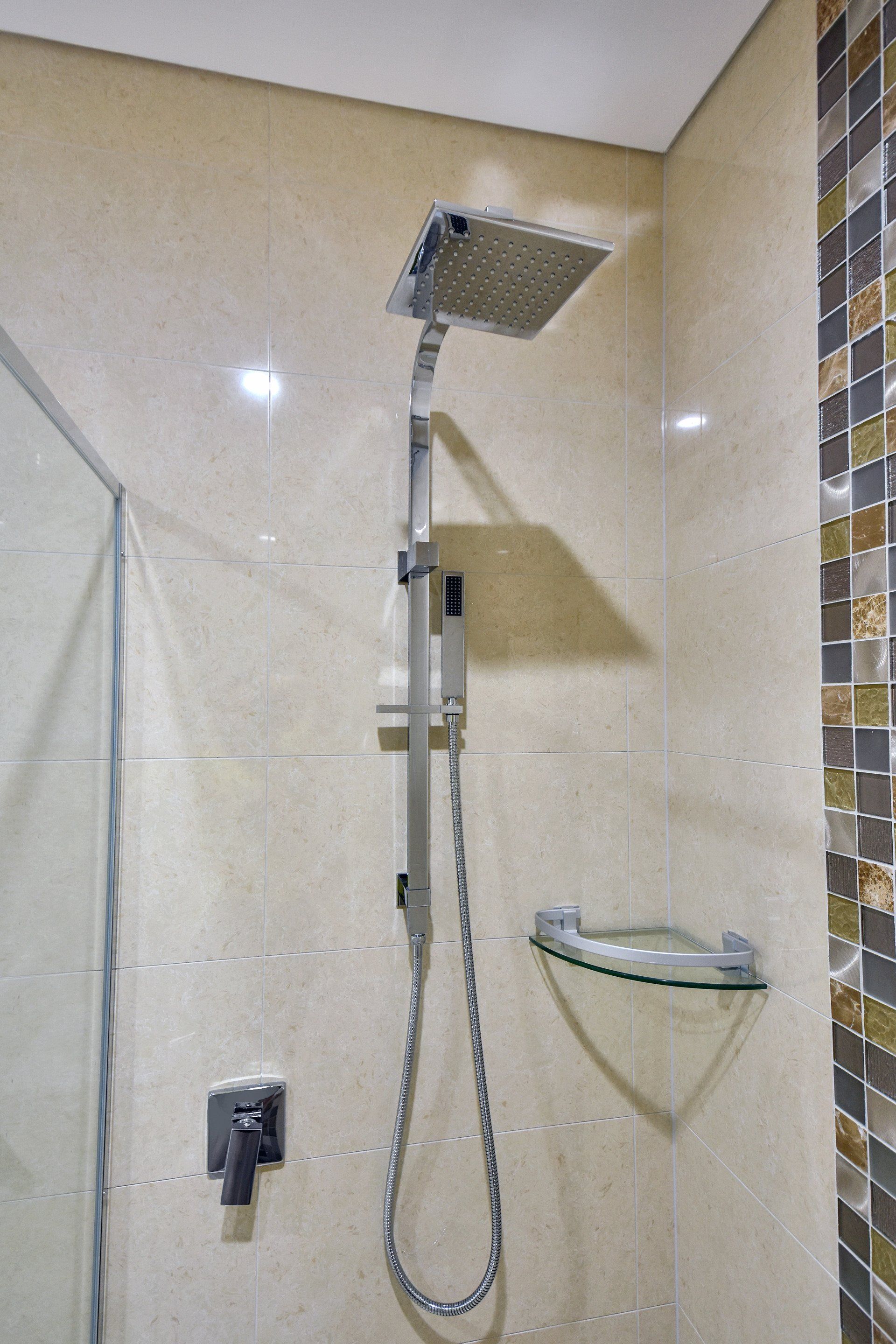 A bathroom with a shower head and a glass shelf.