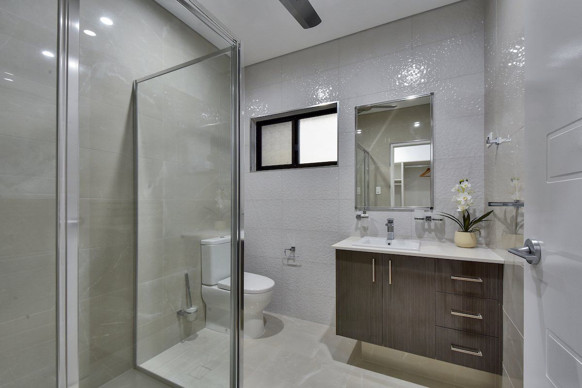 A bathroom with a toilet , sink , mirror and walk in shower.