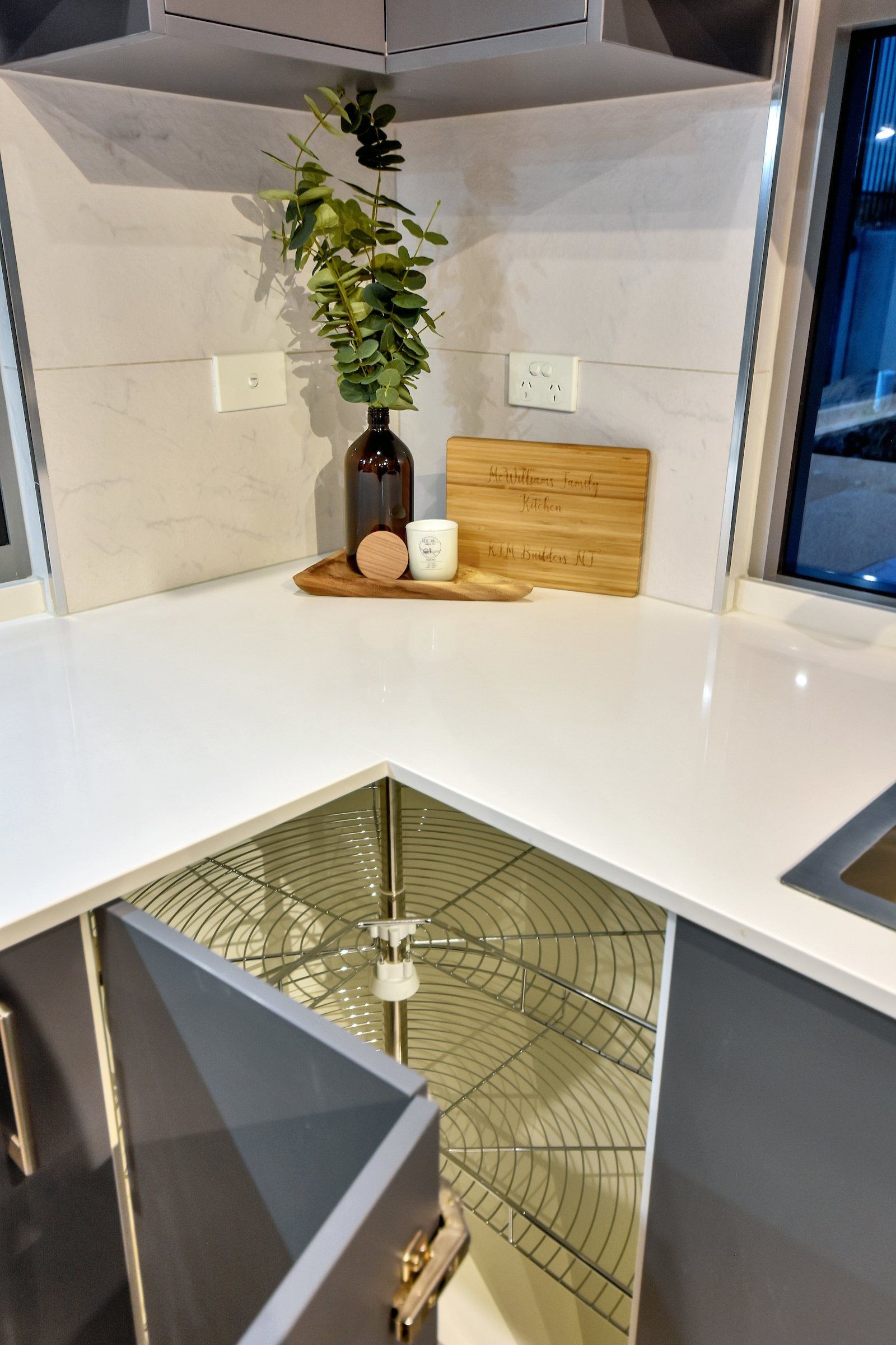A kitchen with a sink , cabinets , a cutting board and a plant on the counter.