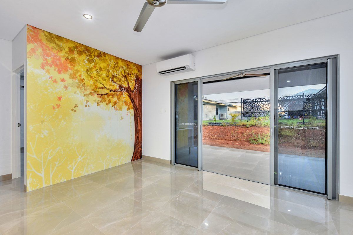 An empty room with a painting of a tree on the wall and a ceiling fan.