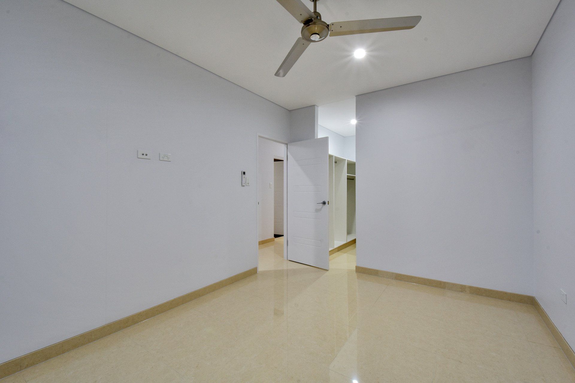 An empty room with a ceiling fan and white walls.
