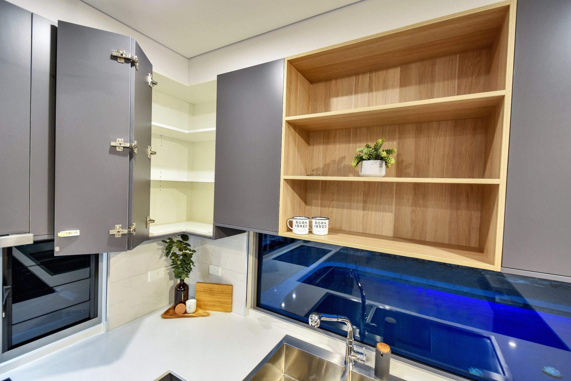 A kitchen with a sink , cabinets , shelves and a window.