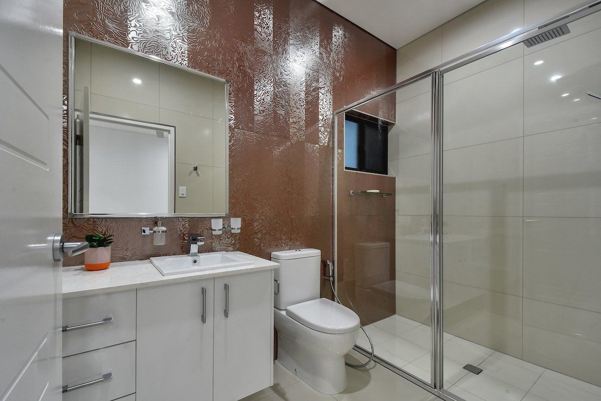 A bathroom with a toilet , sink , mirror and walk in shower.