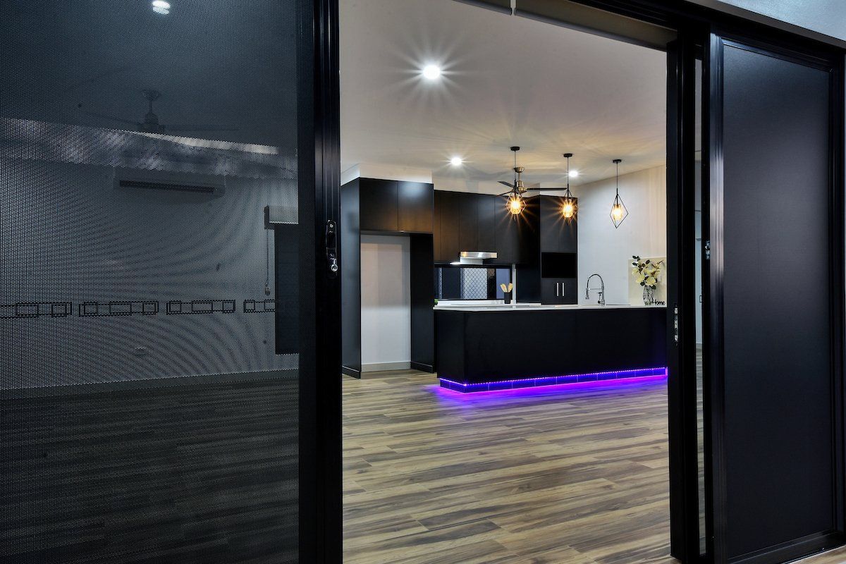 A black door is open to a kitchen with purple lights on the floor.