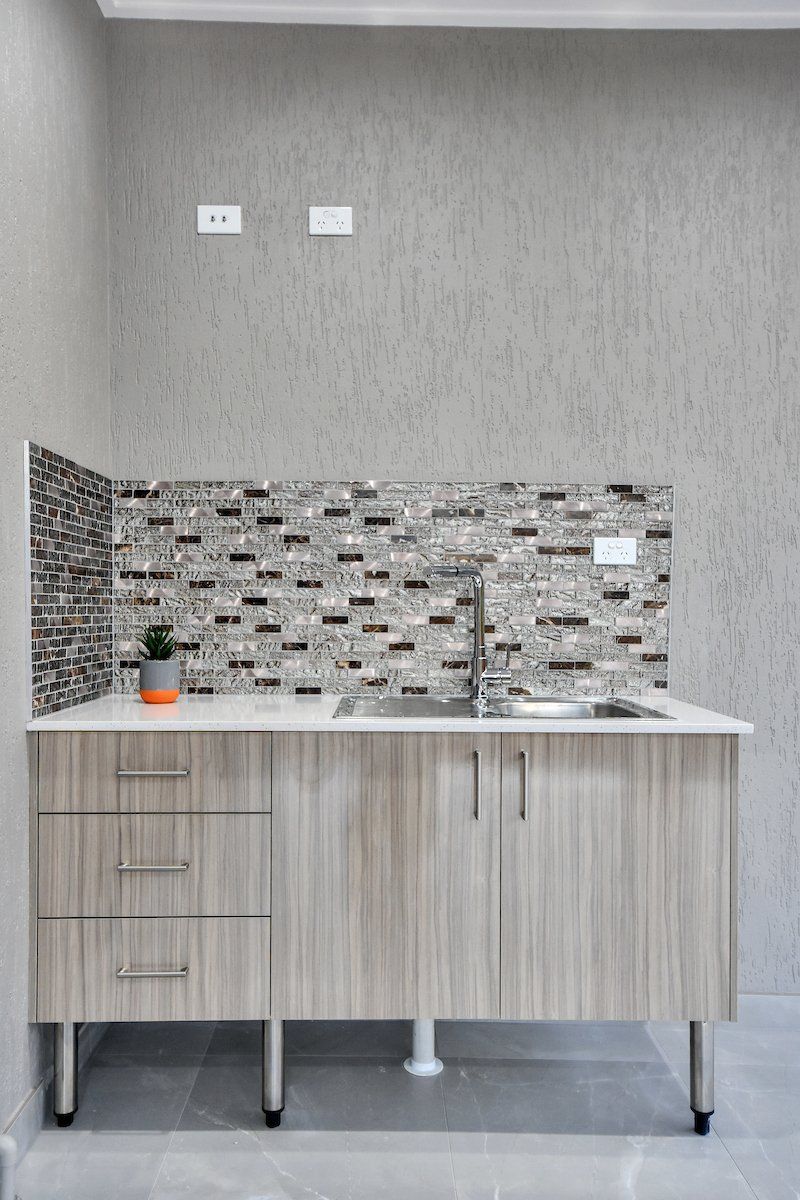 A kitchen with a sink , cabinets and a tiled wall.