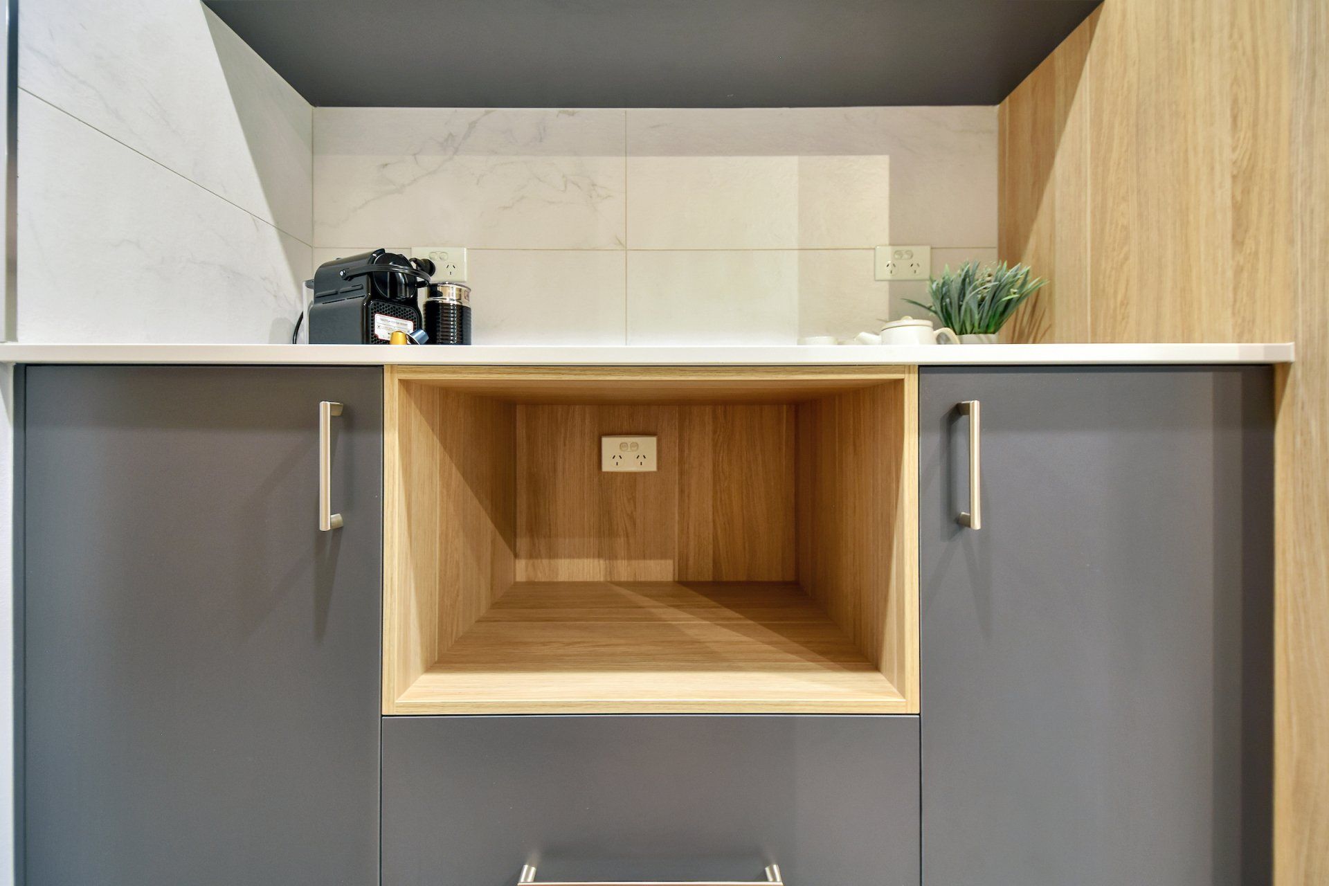 A kitchen with gray cabinets and a wooden shelf in the middle.
