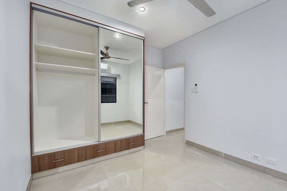 An empty bedroom with a large mirrored wardrobe and a ceiling fan.