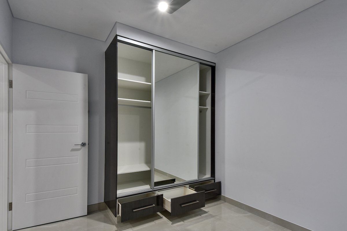 A bedroom with a sliding glass door wardrobe and drawers.