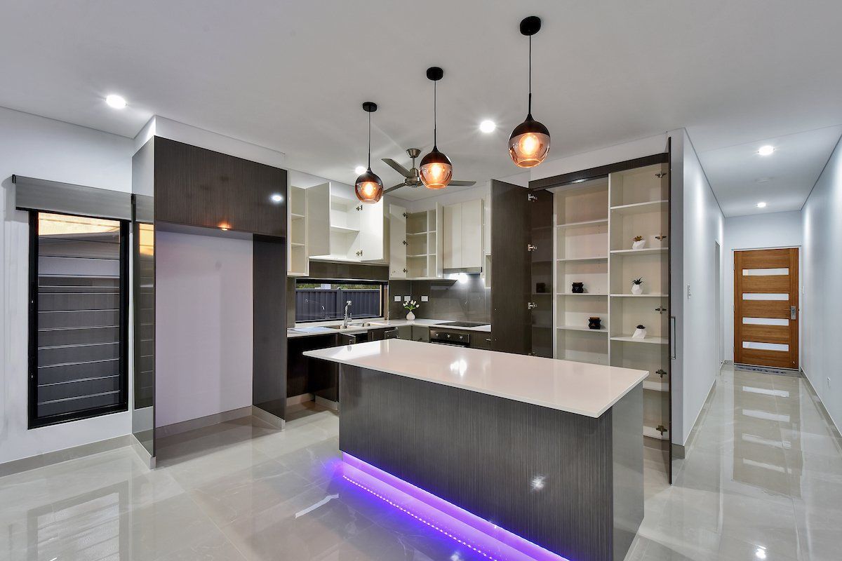 A kitchen with a large island and purple lights on the floor.