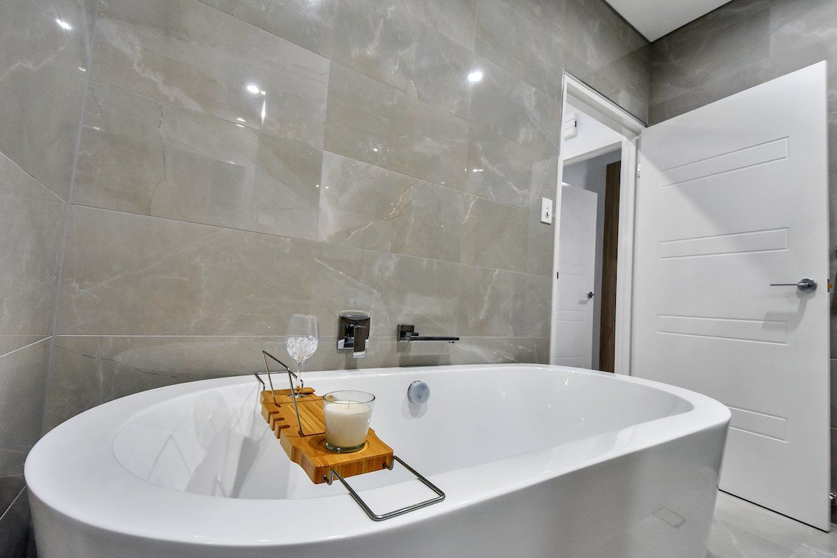 A bathtub with a candle on a wooden tray in a bathroom.