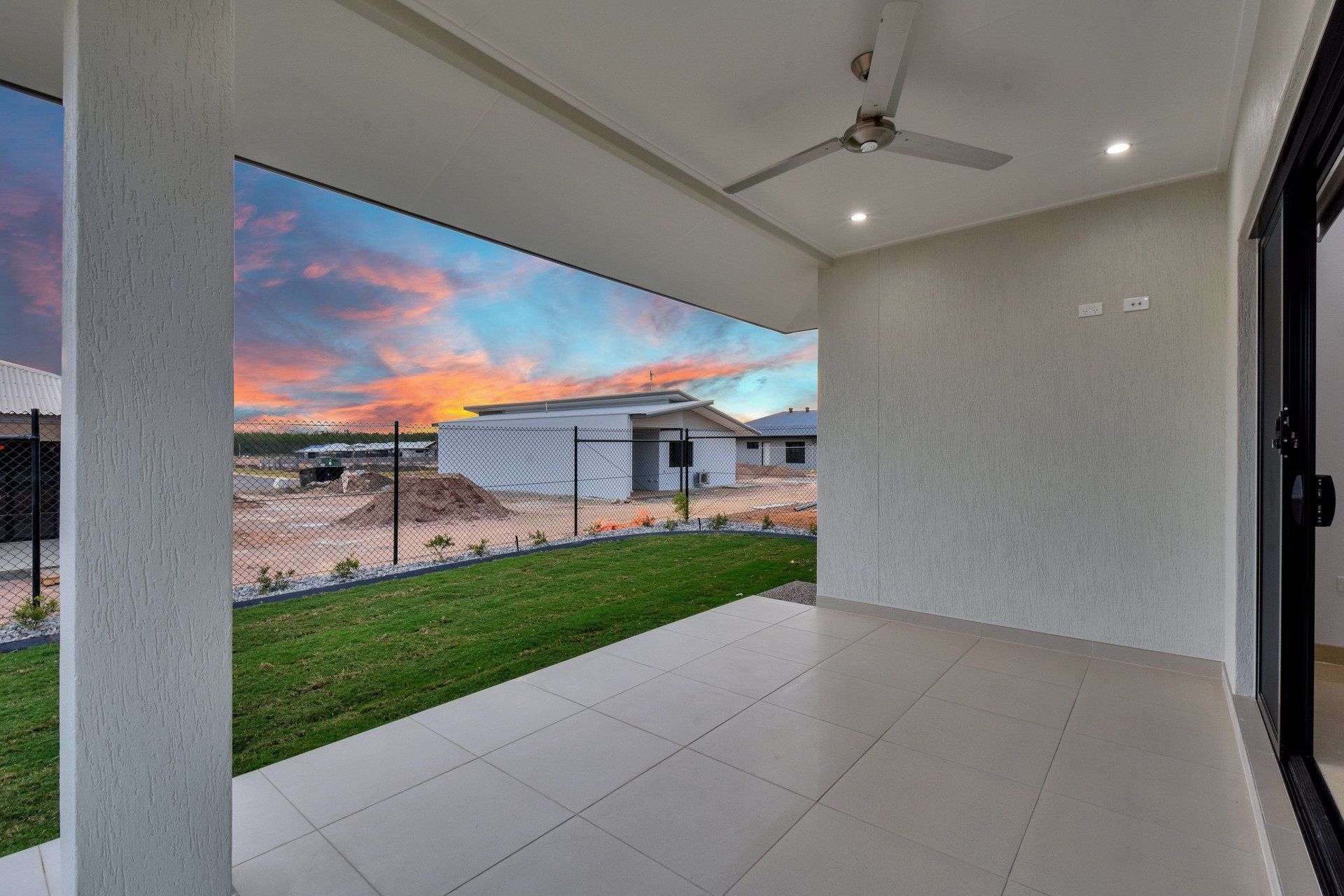 A patio with a ceiling fan and a view of a house under construction.