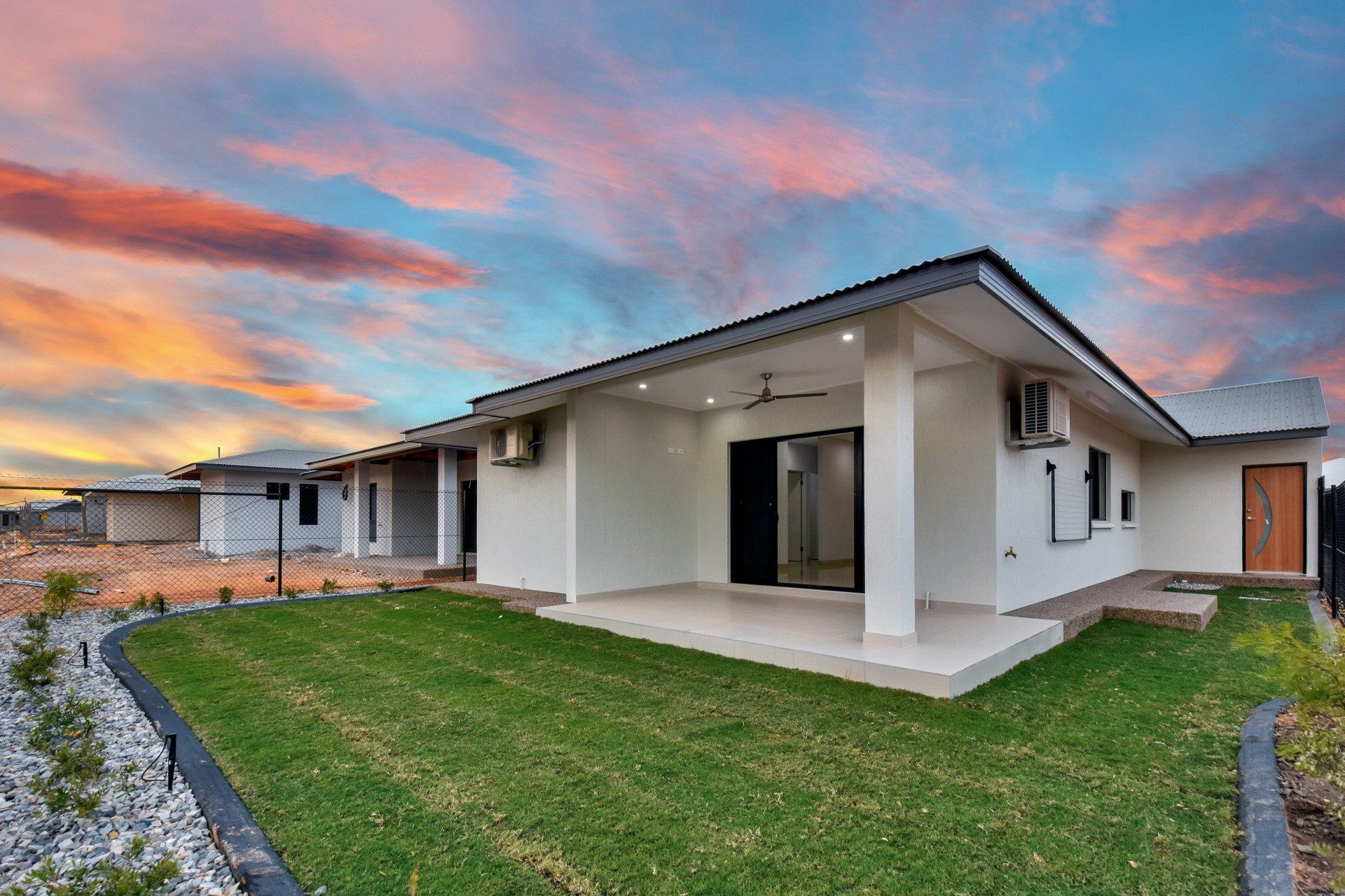 A white house with a large lawn in front of it and a sunset in the background.