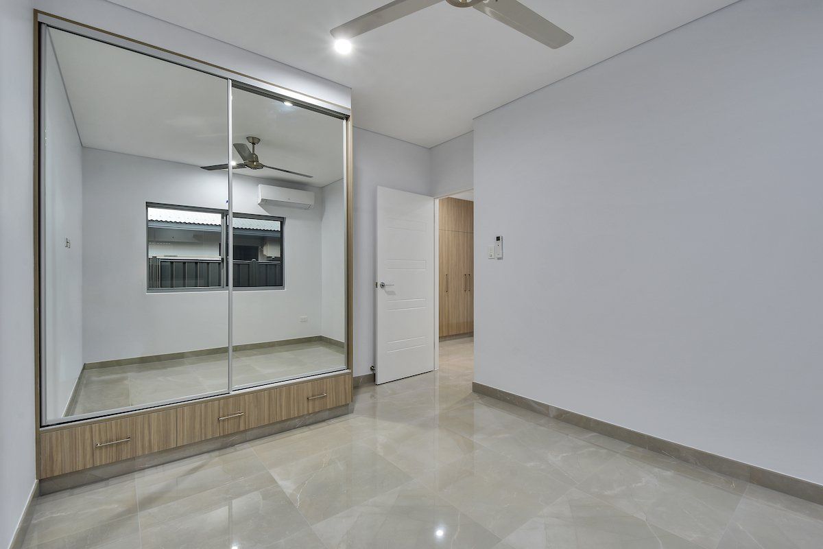 An empty bedroom with a large mirrored wardrobe and a ceiling fan.
