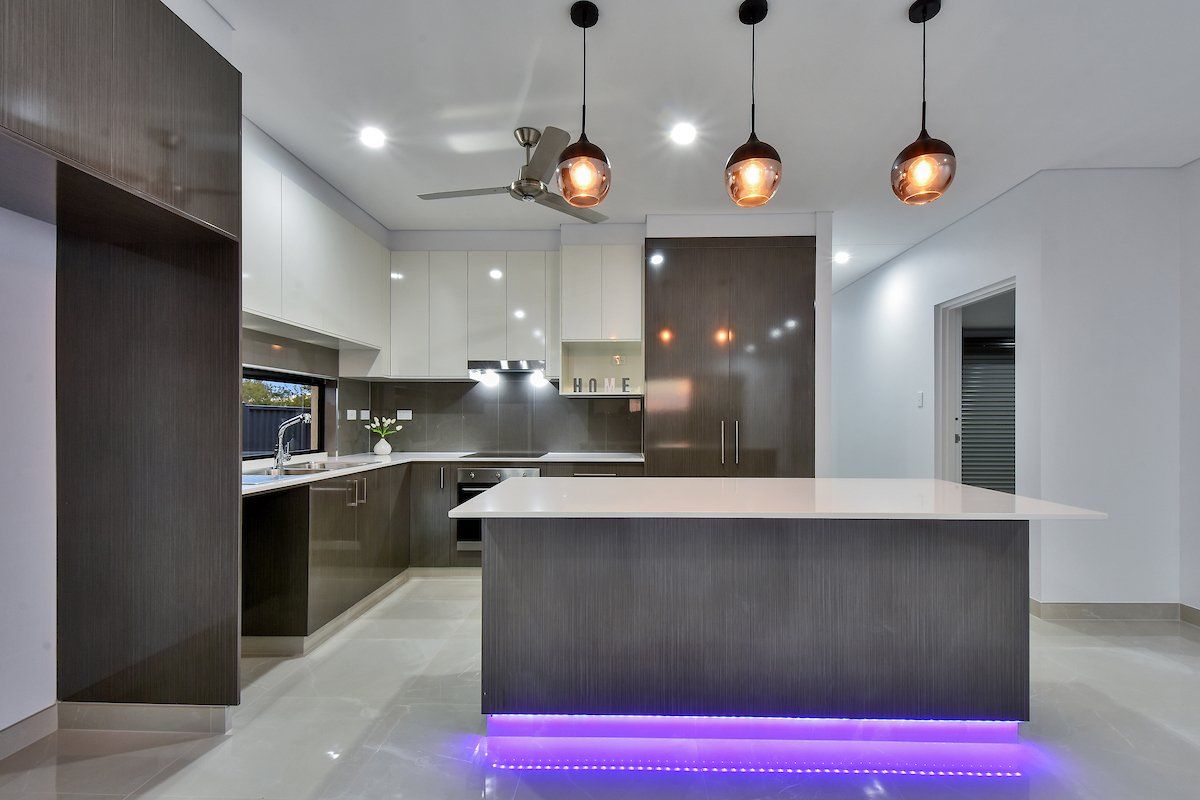 A kitchen with a large island and purple lights on the floor.