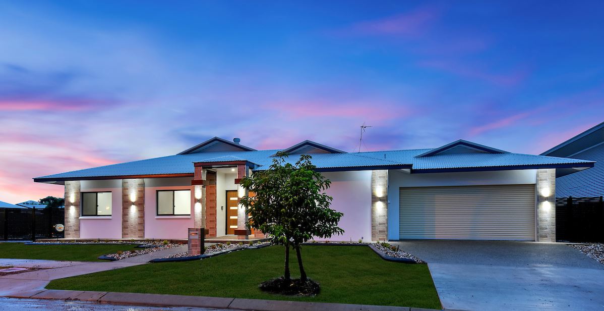 A house with a tree in front of it and a sunset in the background.