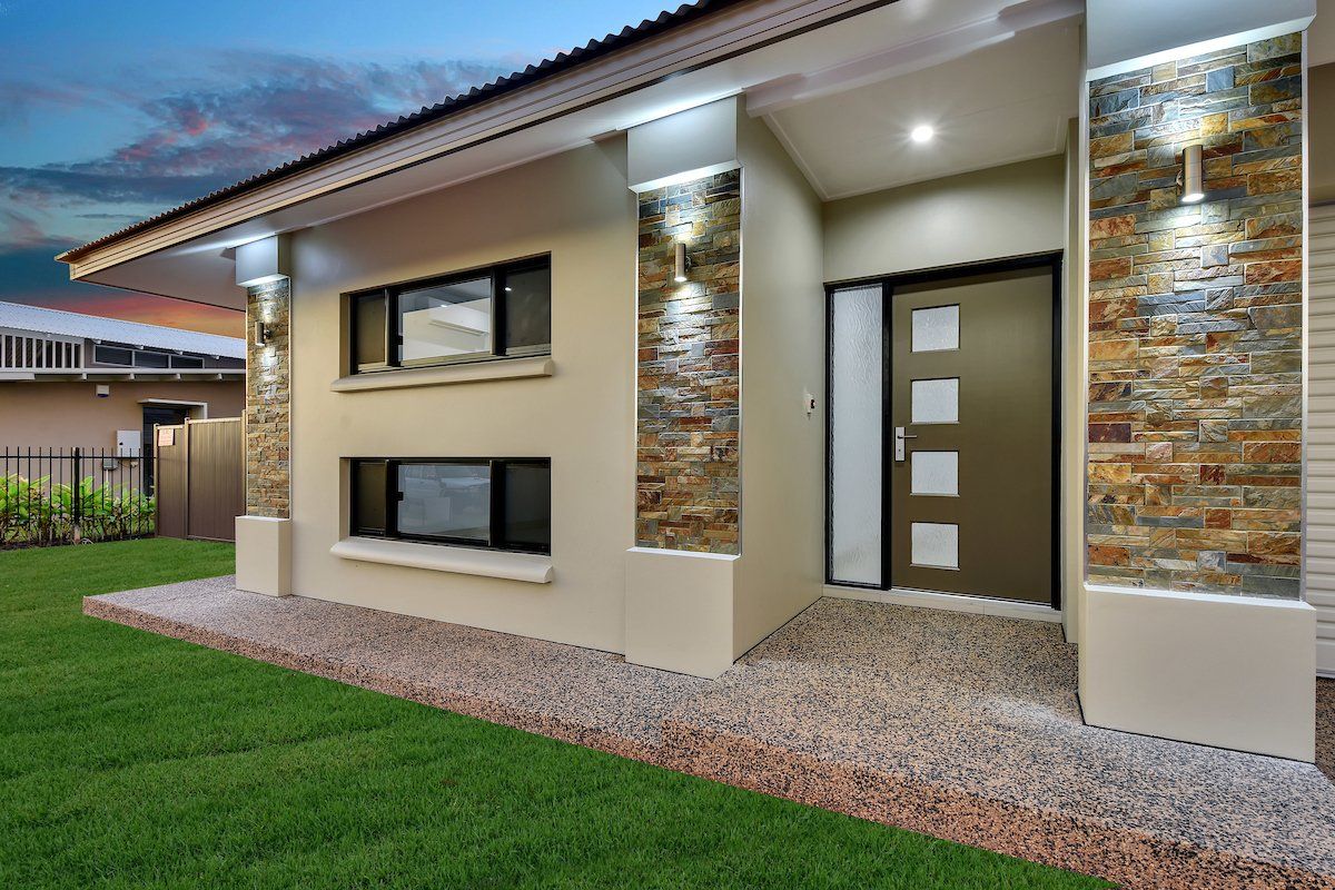 The front of a house with a stone wall and a brown door.