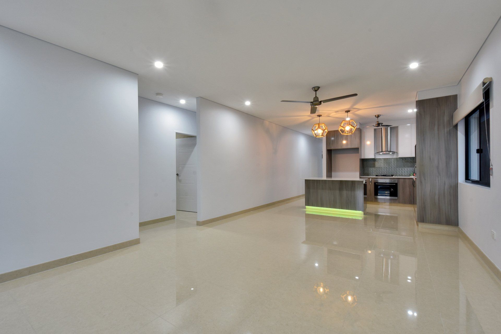 A large empty room with a kitchen and a ceiling fan.