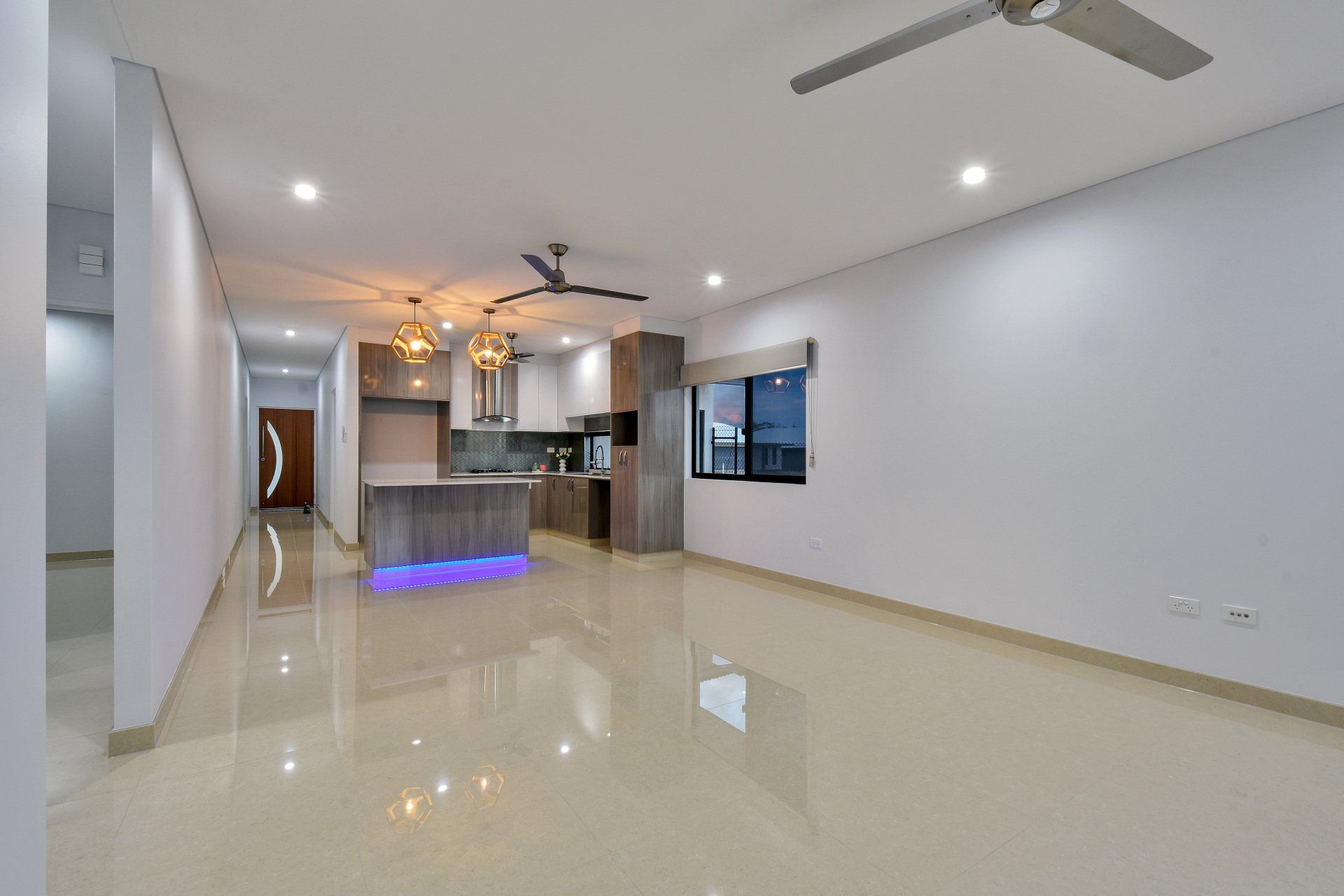 A living room with a ceiling fan and a kitchen in the background.
