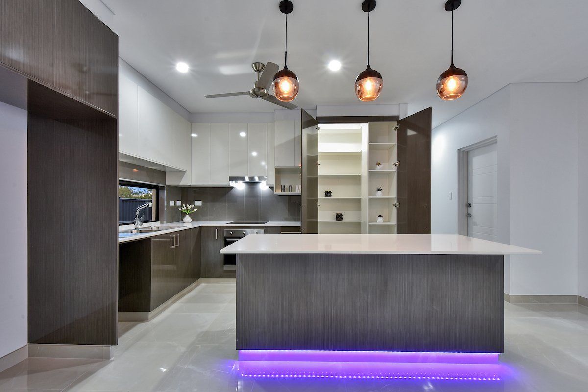 A kitchen with a large island and purple lights on the floor.