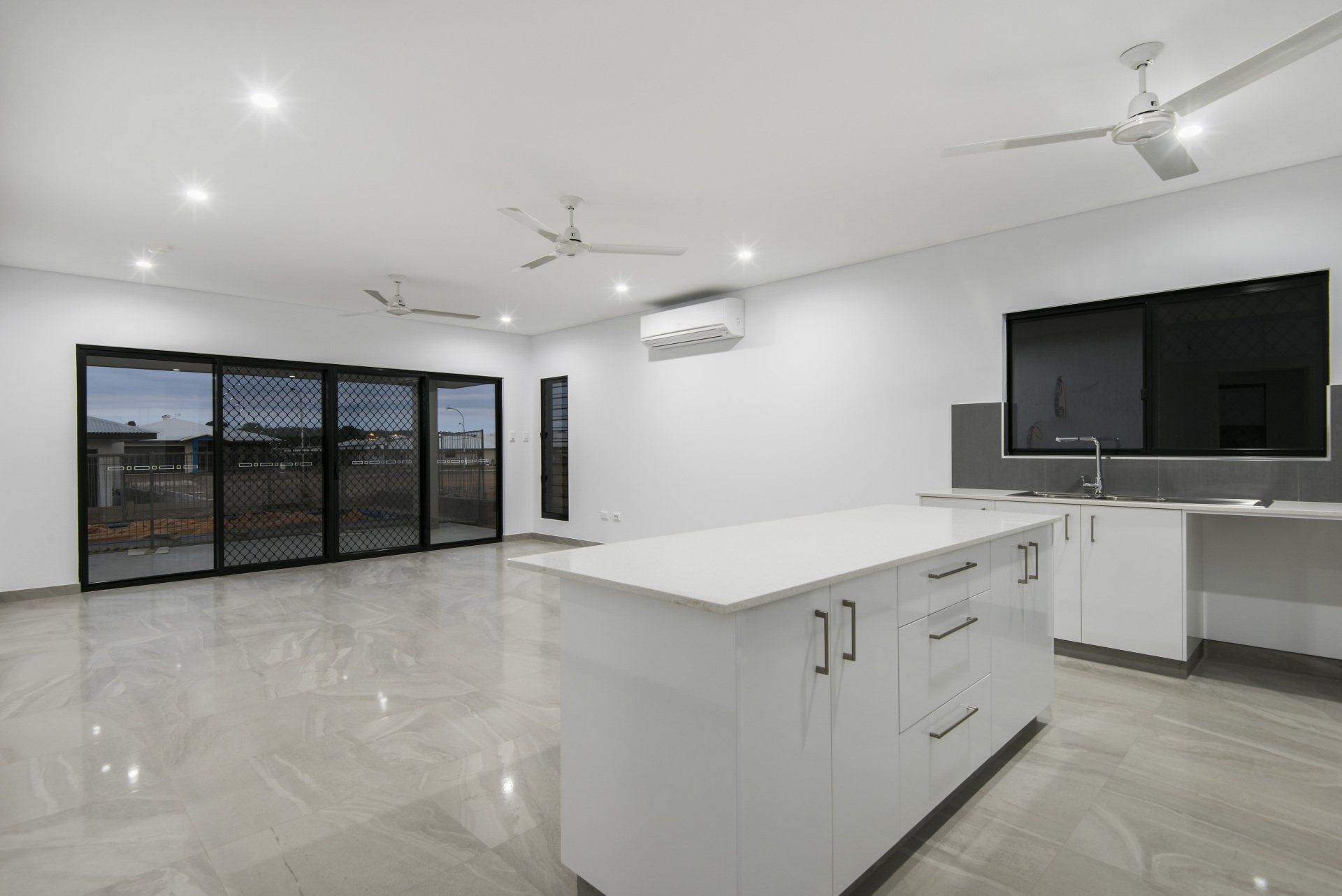 An empty kitchen with a large island and a ceiling fan.