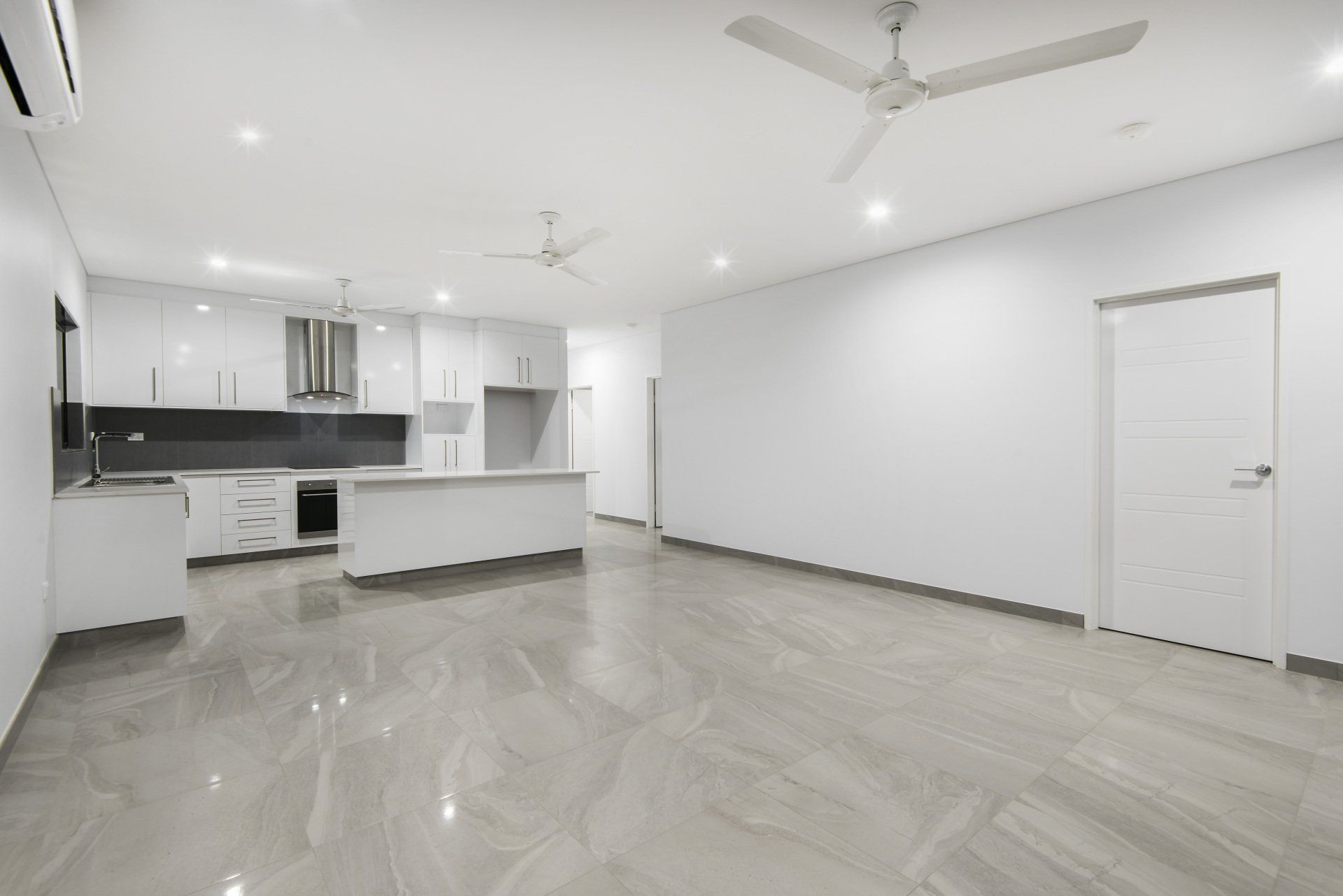 A large empty room with a kitchen and a ceiling fan.