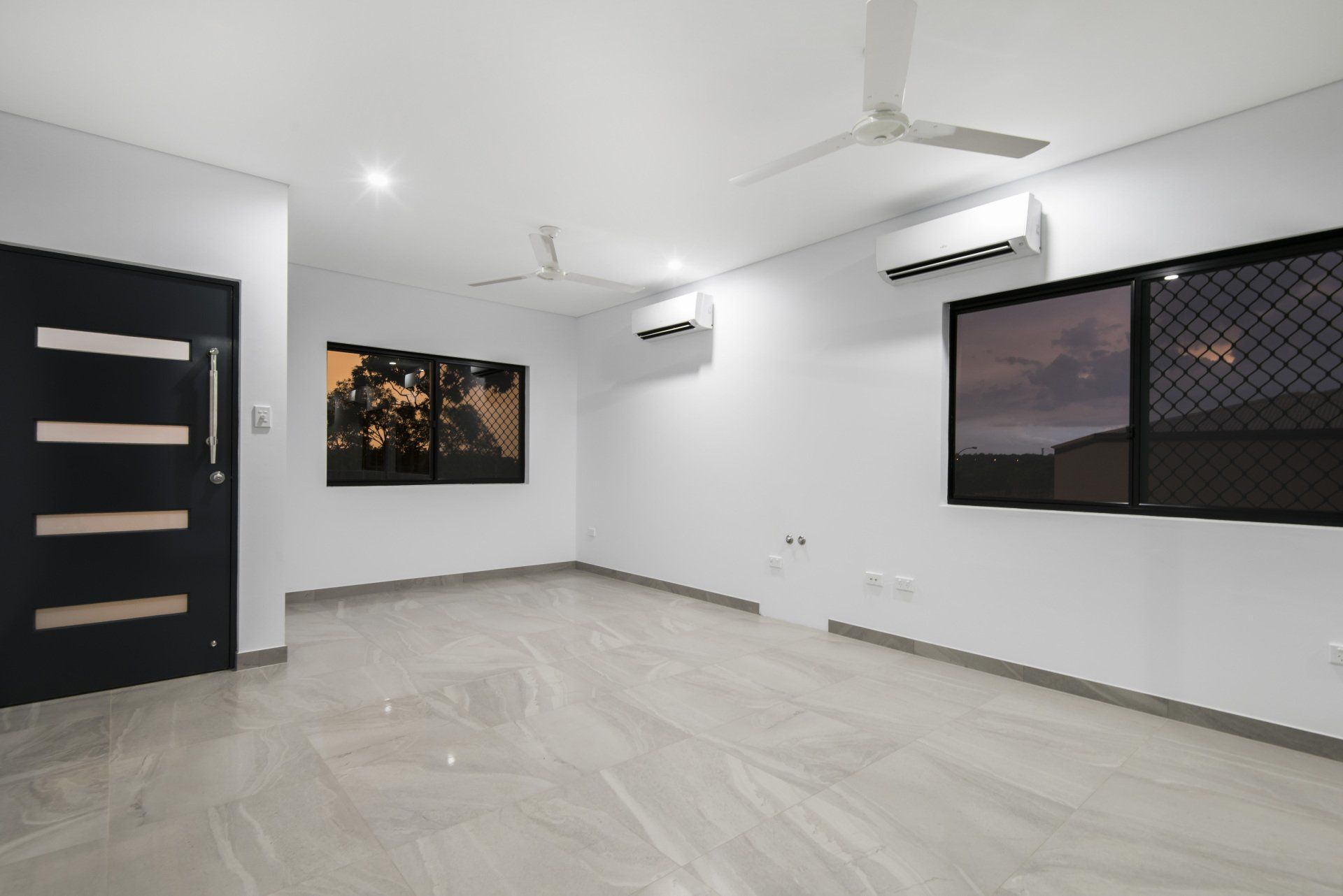 An empty living room with a ceiling fan and two windows.
