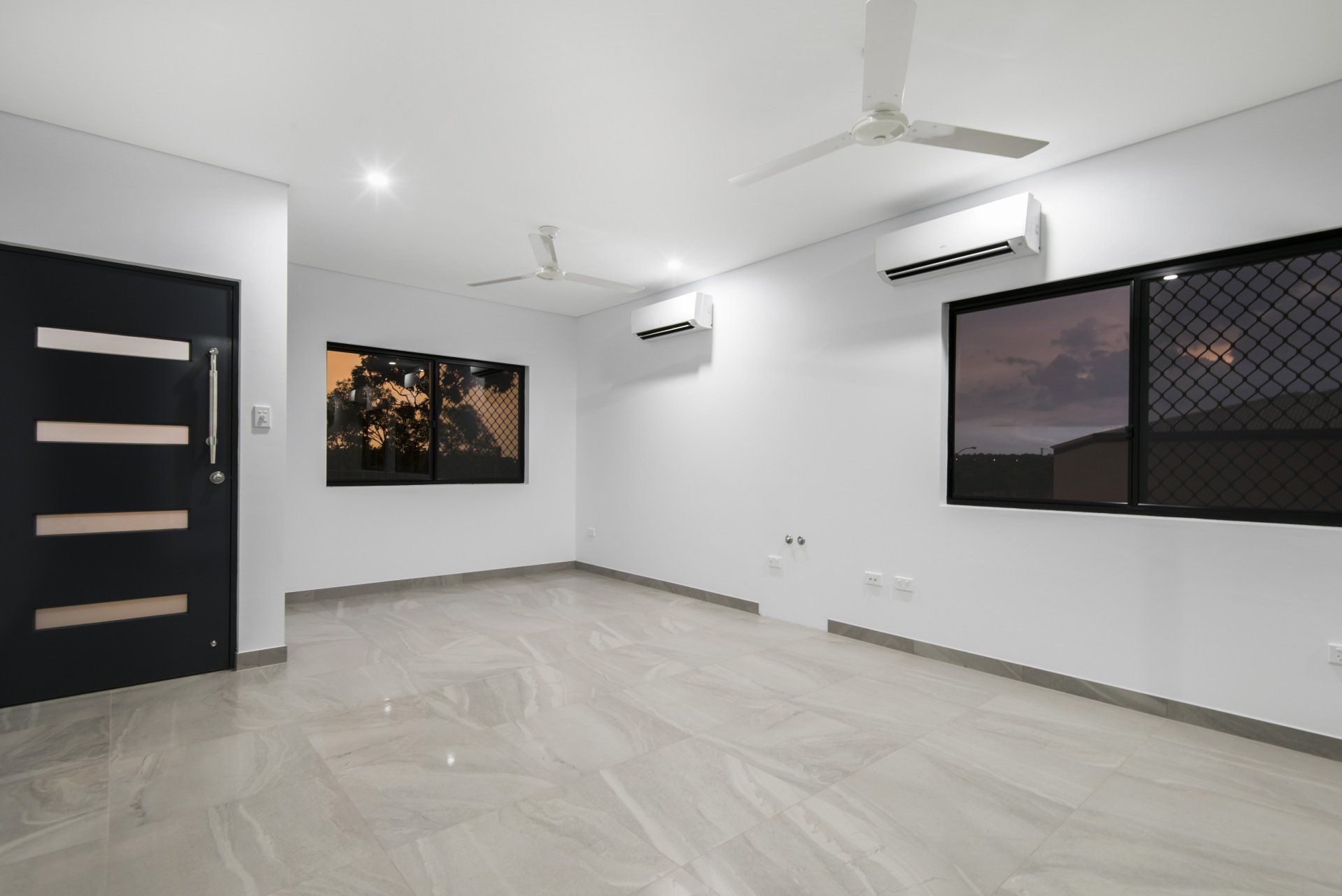 An empty living room with a ceiling fan and two windows.