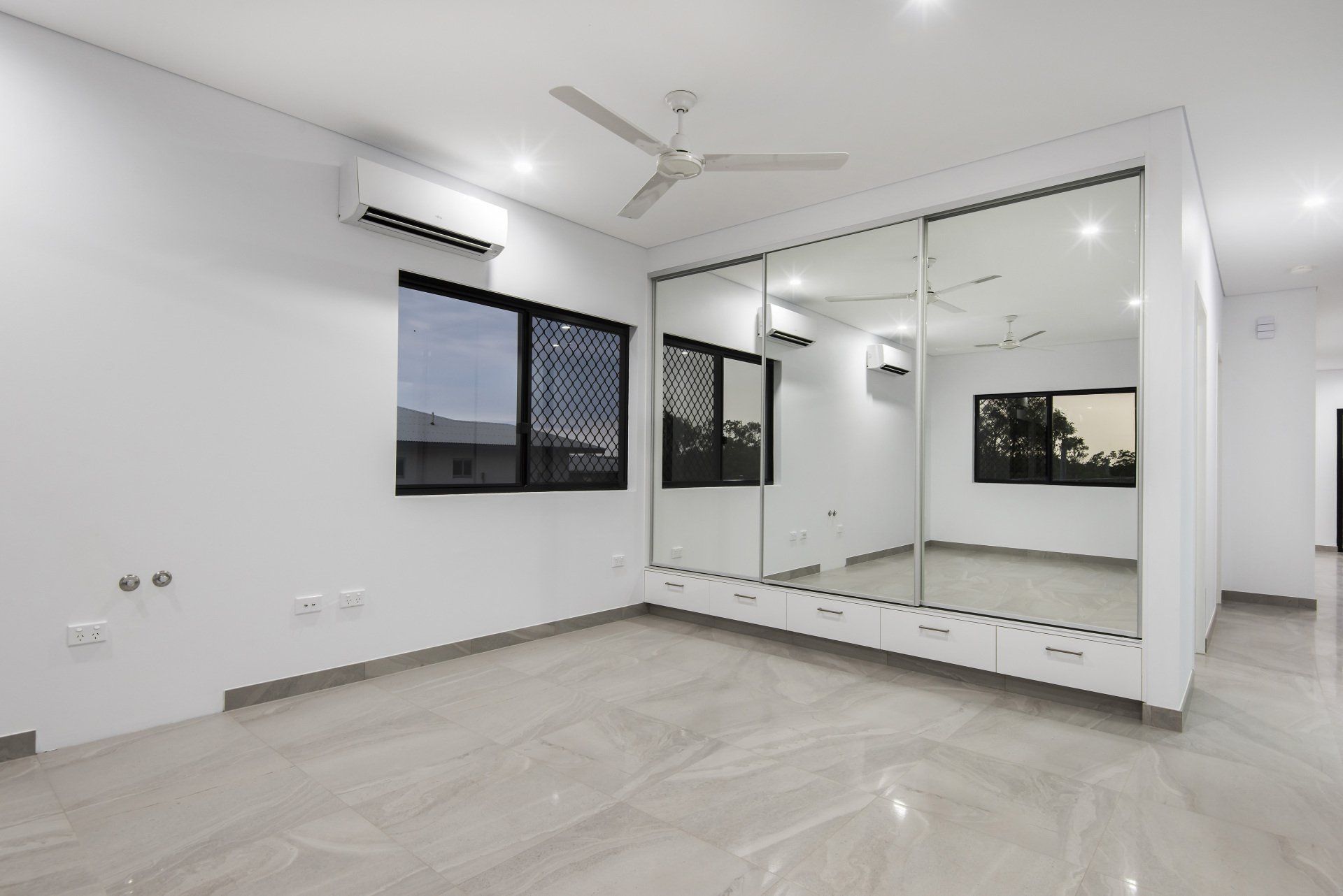 An empty room with a large mirrored wardrobe and a ceiling fan.