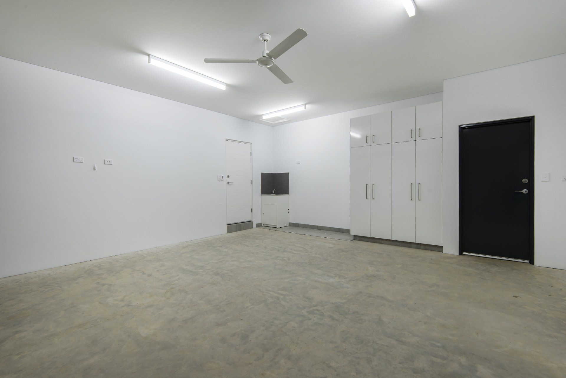 An empty garage with a ceiling fan and a black door.