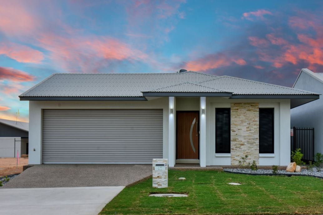 A white house with a gray garage door is sitting on top of a lush green lawn.