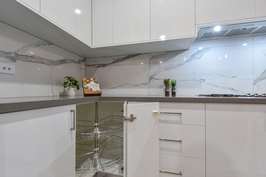 A kitchen with white cabinets and marble counter tops.