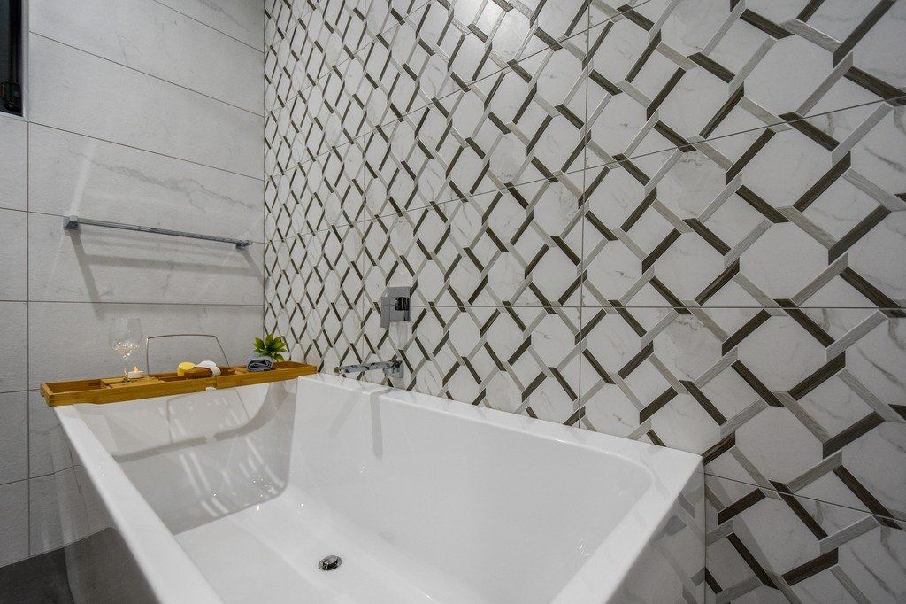 A bathtub in a bathroom with a black and white tile wall.